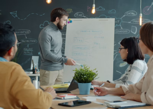Man presenting notes on a flip chart to seated colleagues